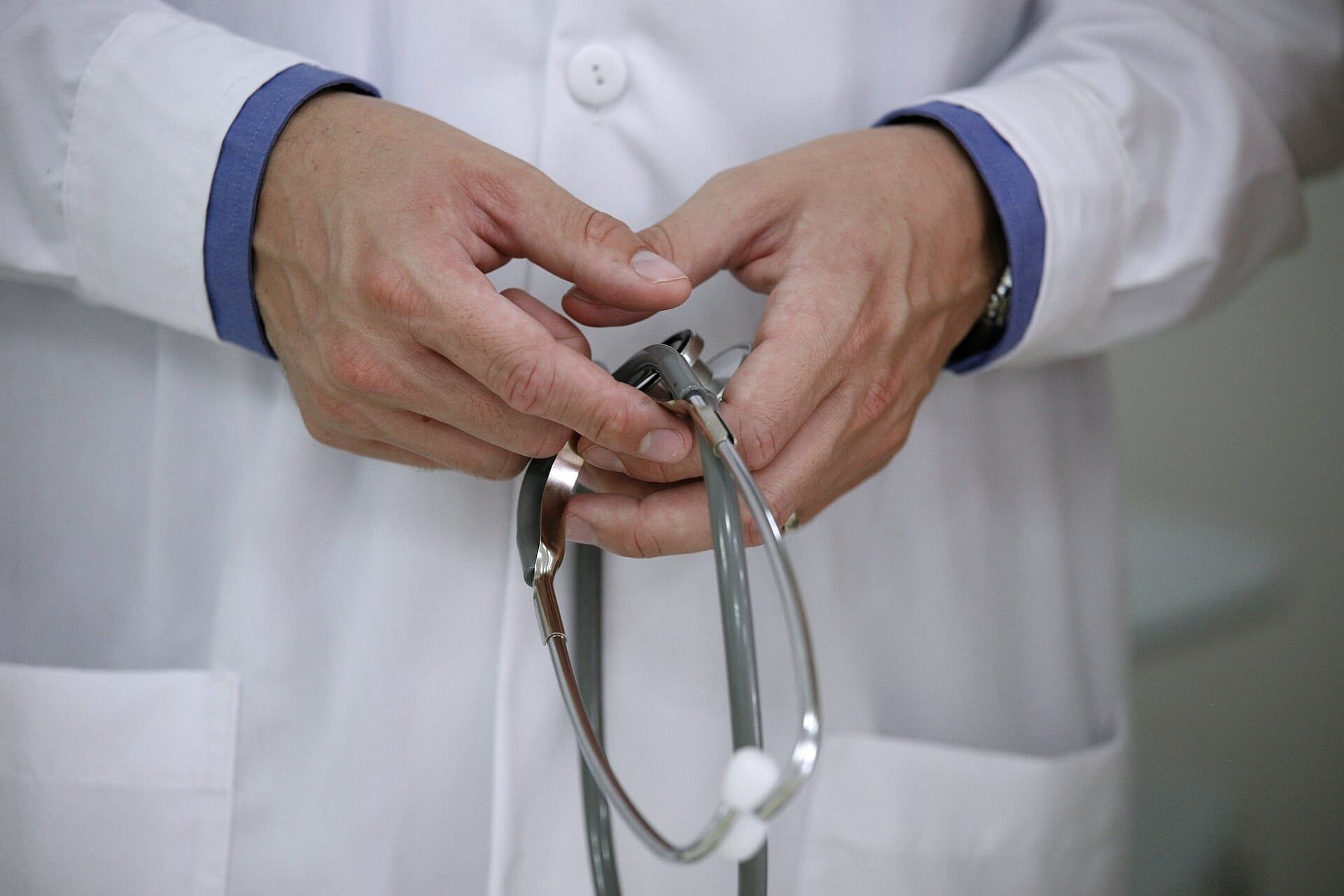 Manos de un médico con guardapolvo blanco sosteniendo un estetoscopio